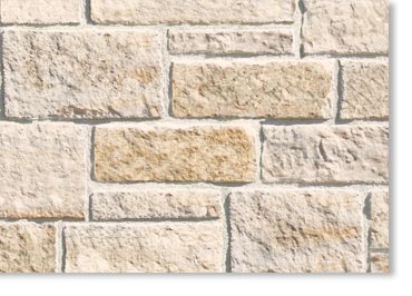 Close-up of a beige brick wall with rough textured stones and light gray mortar between bricks.