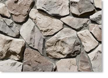 Close-up of irregular beige and gray stones forming a rustic stone wall with rough textures.