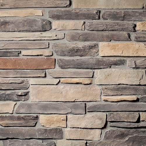 Close-up of a stacked stone wall with irregular rectangular stones in gray, beige, and brown.