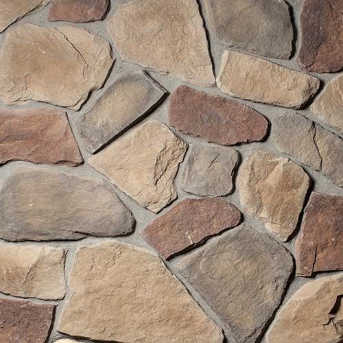 Close-up of a beige, brown, and gray stone wall with irregular shapes and light mortar lines across the surface; a rustic masonry detail.