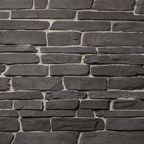 Close-up of a dark gray stacked stone wall with uneven rectangular stones and light mortar lines.