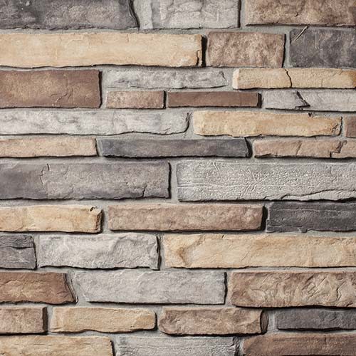 Stacked stone wall with irregular rectangular stones in tan, gray, and brown tones.