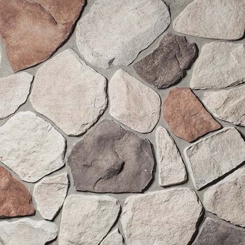 Close-up of irregular gray, white, and brown stones fitted together in a stone wall edge-to-edge surface.