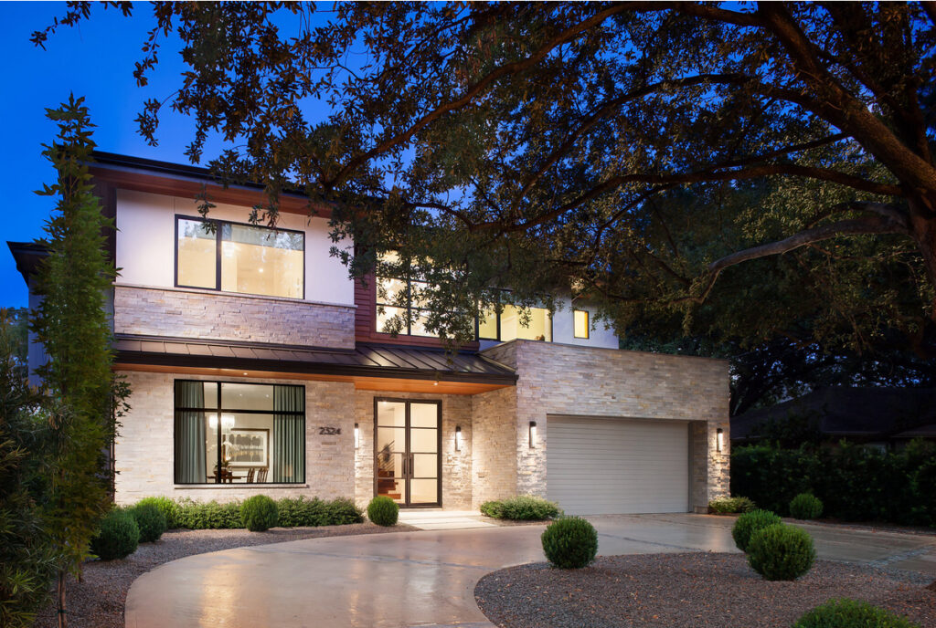 Modern two-story house with stone facade, illuminated entryway, and a closed garage at dusk.