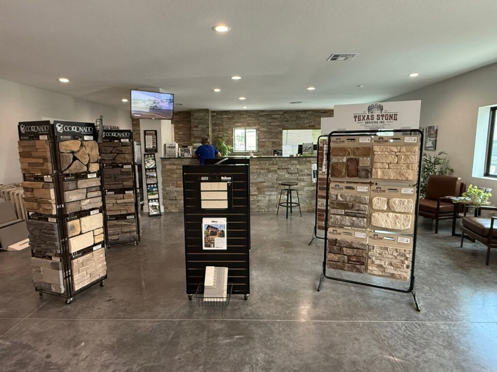 Showroom with stone veneer sample displays on racks left and right and a reception counter in the back.