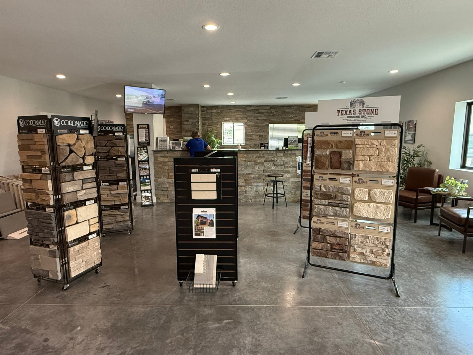 Showroom with stone veneer sample displays on racks left and right and a reception counter in the back.